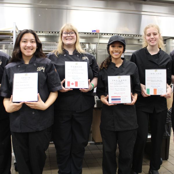  students in black chef attire hold frames