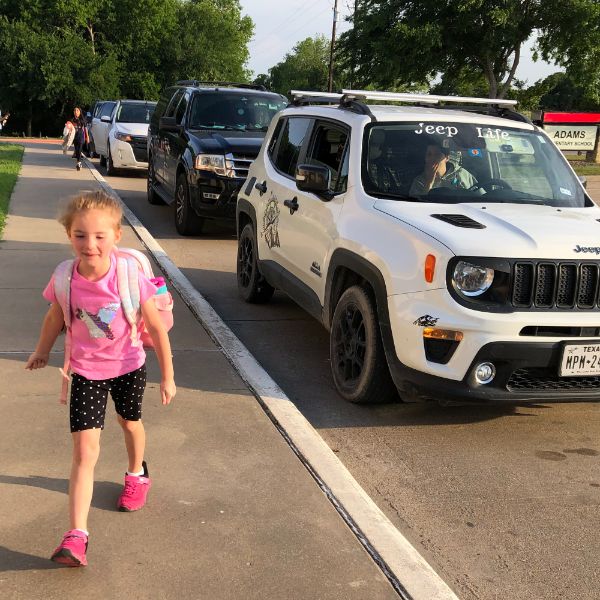  little girl walking with line of cars in background